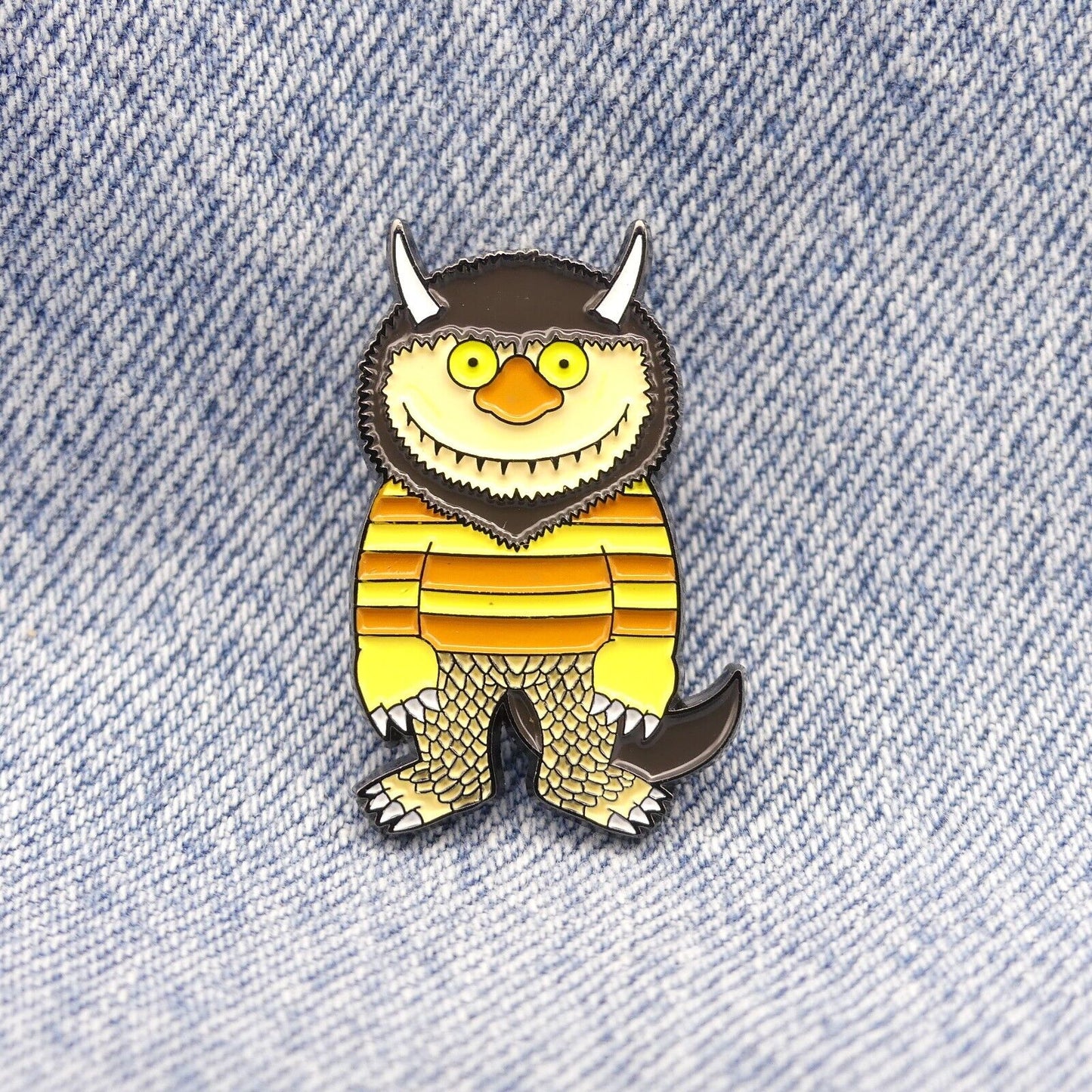 Enamel pin badge showing a grinning yellow monster with striped orange body and brown tail.