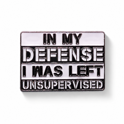 Enamel pin badge close-up with "IN MY DEFENSE" quote, black outline and silver rim