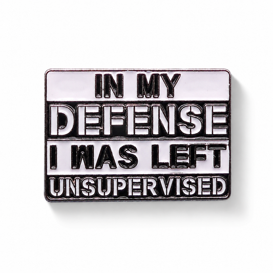 Enamel pin badge close-up with "IN MY DEFENSE" quote, black outline and silver rim