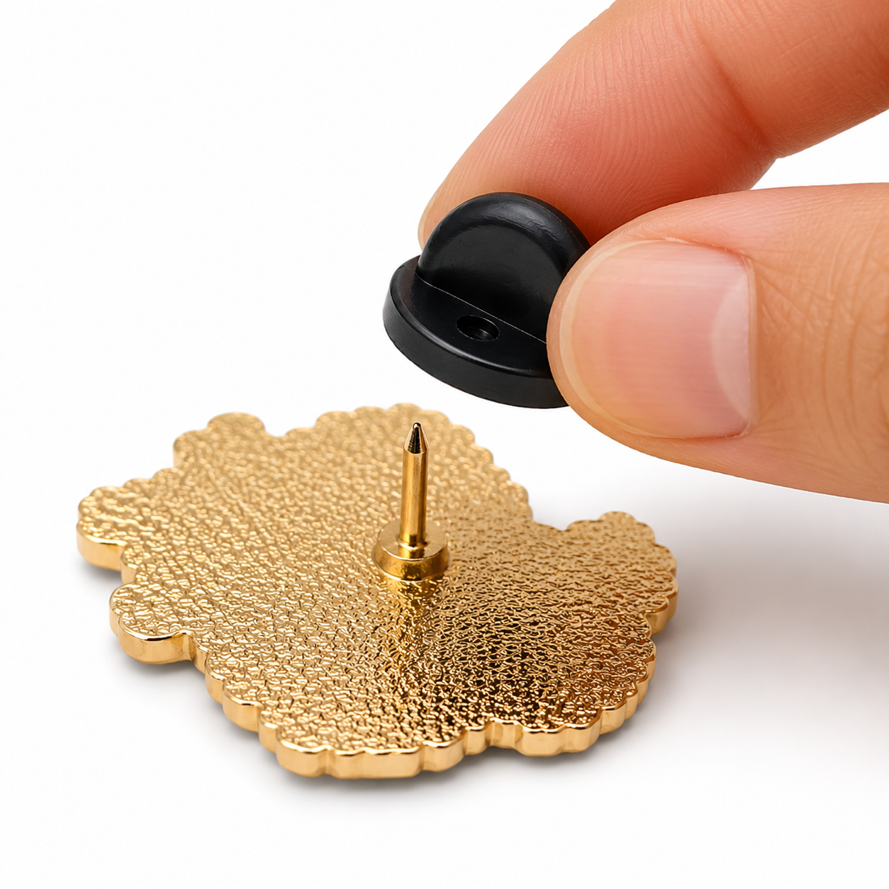 Gold pin with black rubber pin back being pressed onto a finger