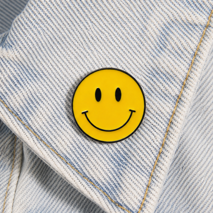 Yellow smiley face enamel pin badge close-up on light blue denim
