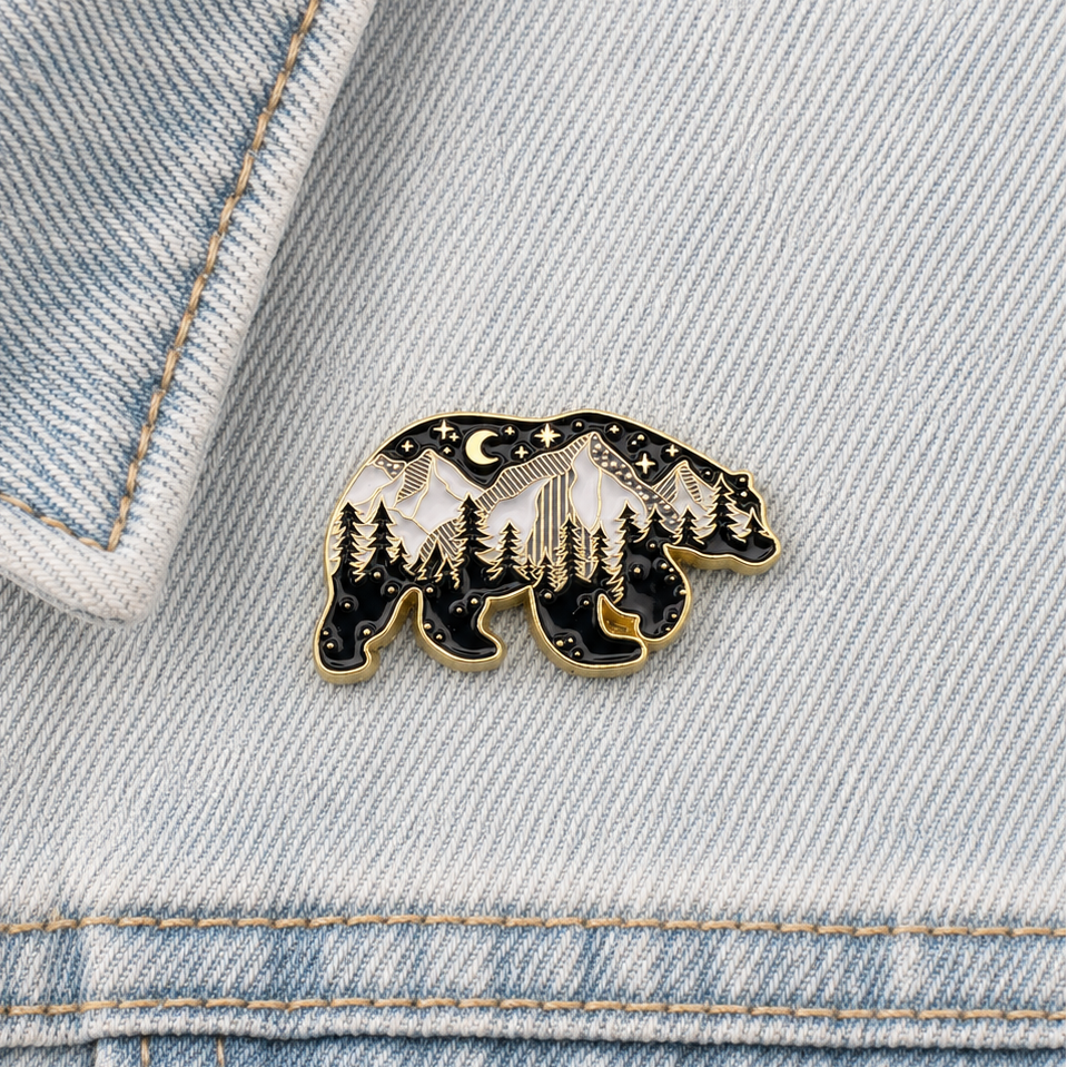 Small black bear enamel pin with forest trees and starry sky, gold edging