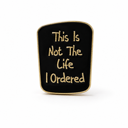 Gold-rim enamel pin badge with black quote: “This Is Not The Life I Ordered”