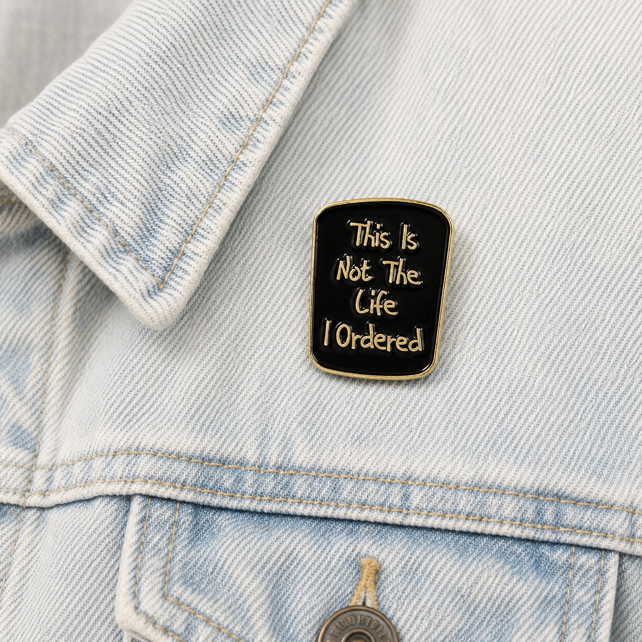 Enamel pin badge on light blue denim jacket, black with gold quote and border