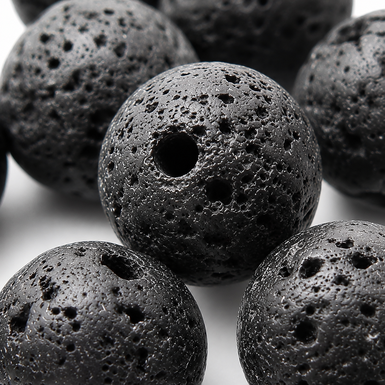 Close-up of black round lava stone beads with rough texture and drilled holes