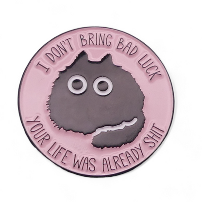 A round enamel pin badge featuring a black cat with wide eyes on a pink background, with the humorous message 'I DON'T BRING BAD LUCK YOUR LIFE WAS ALREADY SH*T'.