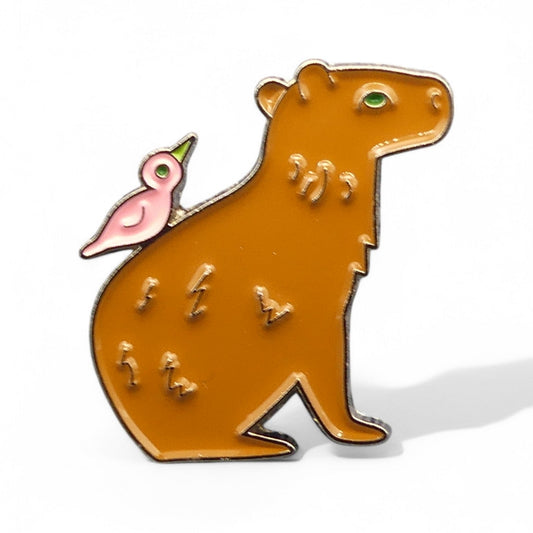 Enamel pin of a brown capybara rodent with a pink bird sitting on its back.