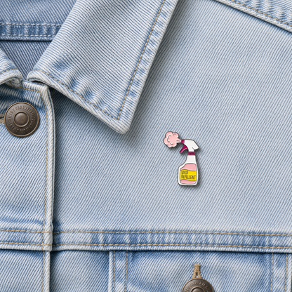 Enamel pin badge featuring a spray bottle and pink cloud face on light blue denim