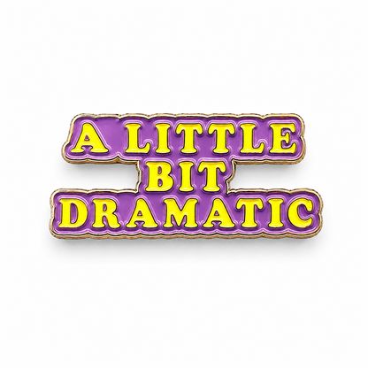Purple enamel text badge pin reading “A LITTLE BIT DRAMATIC” with gold border.