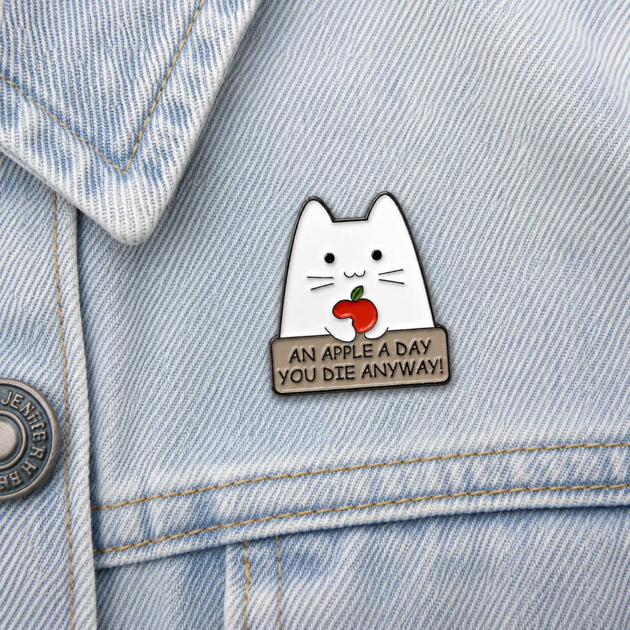 Cat enamel pin badge on light blue denim, white cat with red apple and dark text