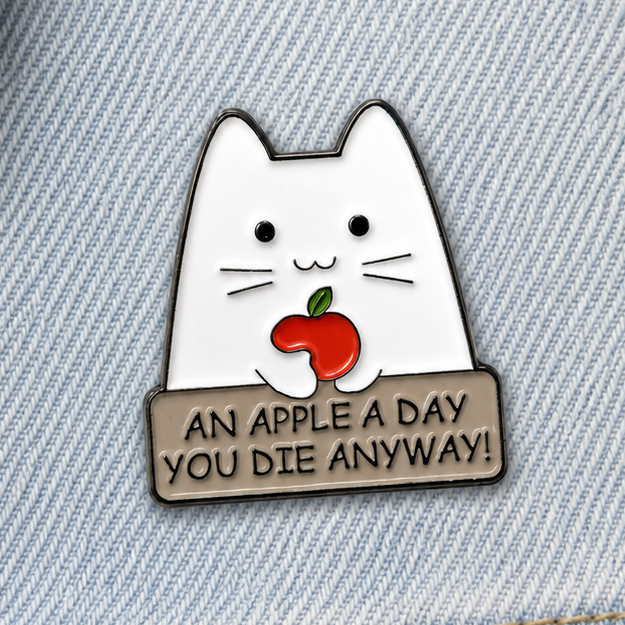 Cat enamel pin badge on light blue denim, white cat with red apple and dark slogan