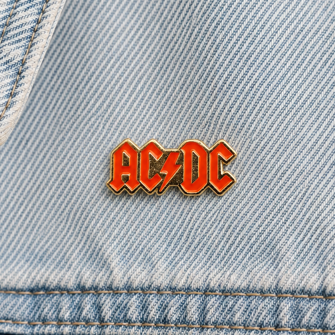 Small AC/DC enamel pin on light blue denim, red logo letters with gold trim