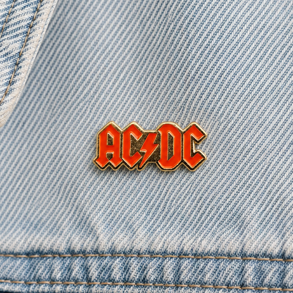 Small AC/DC enamel pin on light blue denim, red logo letters with gold trim
