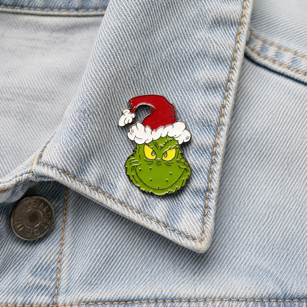 Green character enamel pin with red Santa hat and white beard on light blue denim