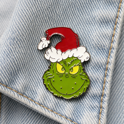 Green character enamel pin badge with red Santa hat and white beard on denim close-up