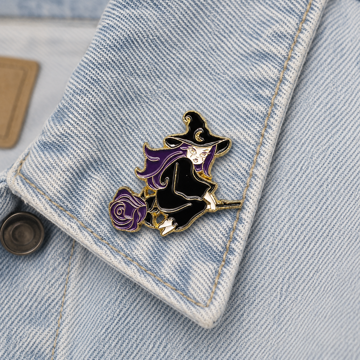 Witch on broom enamel pin with purple rose on light blue denim pocket