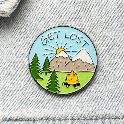 Get Lost enamel pin badge close-up with mountains, trees and campfire scene.