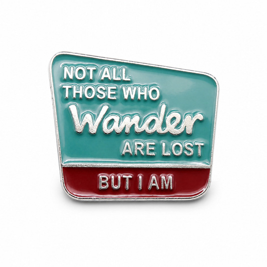 Square enamel pin badge in teal and red with 'Wander' quote text