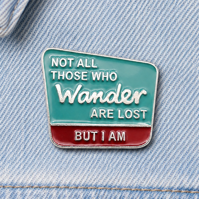 Enamel quote pin badge on light blue denim, teal and red 'Wander' design