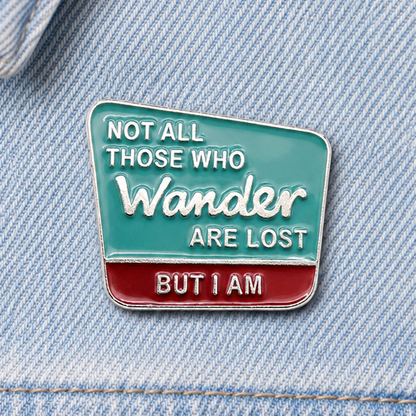 Enamel quote pin badge on light blue denim, teal and red 'Wander' design