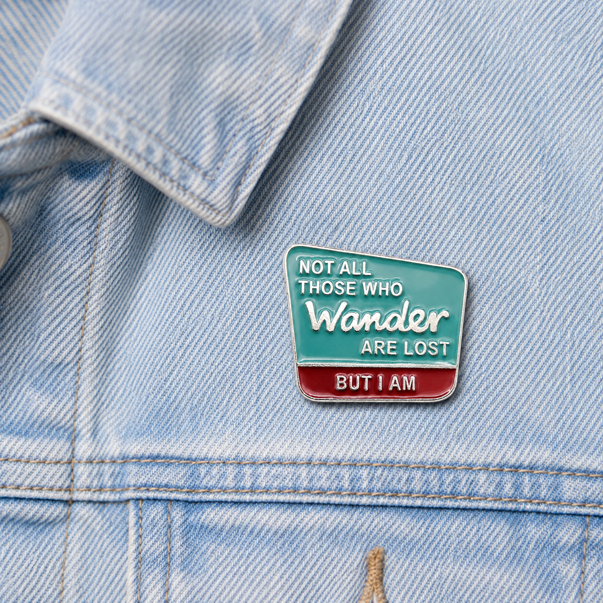 Small enamel pin badge on light blue denim jacket, teal and red 'Wander' quote