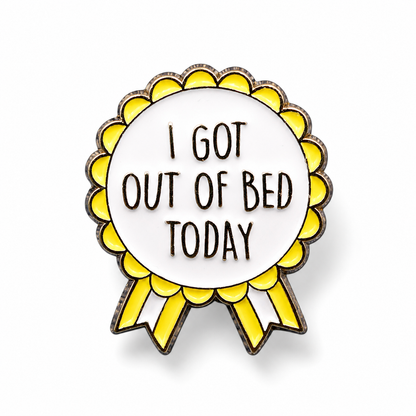 Yellow rosette enamel pin with white center and black text, 'I GOT OUT OF BED TODAY'