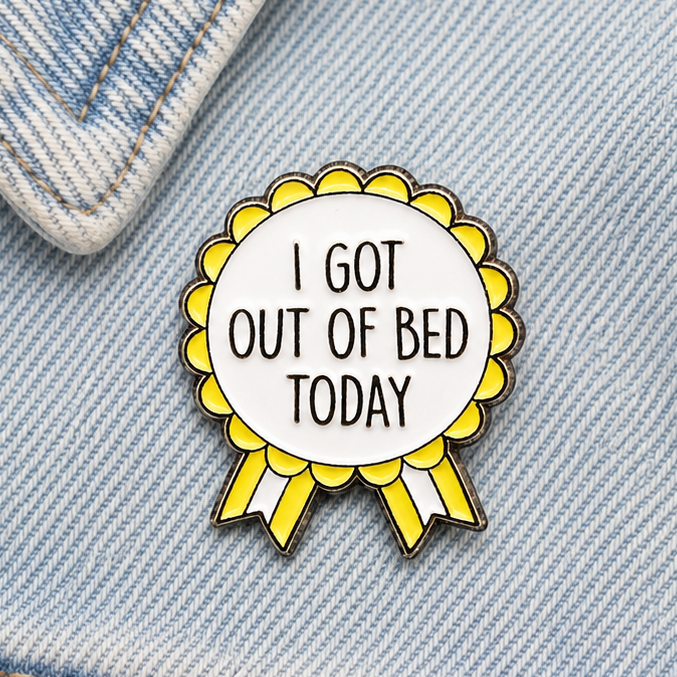 Yellow rosette enamel pin on blue denim, white center with 'I GOT OUT OF BED TODAY'