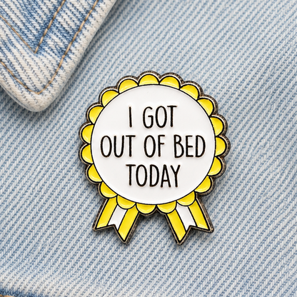 Yellow rosette enamel pin on blue denim, white center with 'I GOT OUT OF BED TODAY'