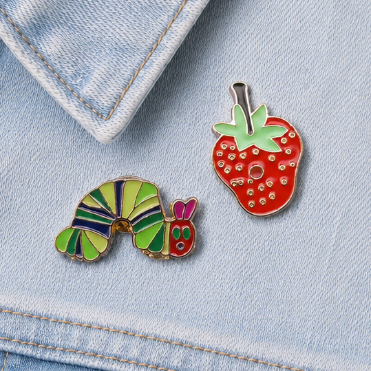 Close-up of strawberry and caterpillar enamel pin badges on denim