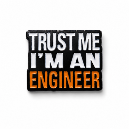 Enamel pin badge reading “TRUST ME I'M AN ENGINEER” on black and orange