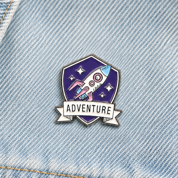 Purple rocket adventure enamel pin badge on light blue denim, close-up front view