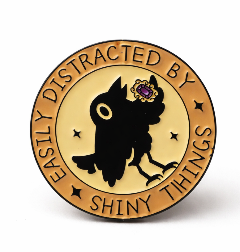 Circular badge pin badge with crow  holding a jewel design and text 'Easily Distracted by Shiny Things' 