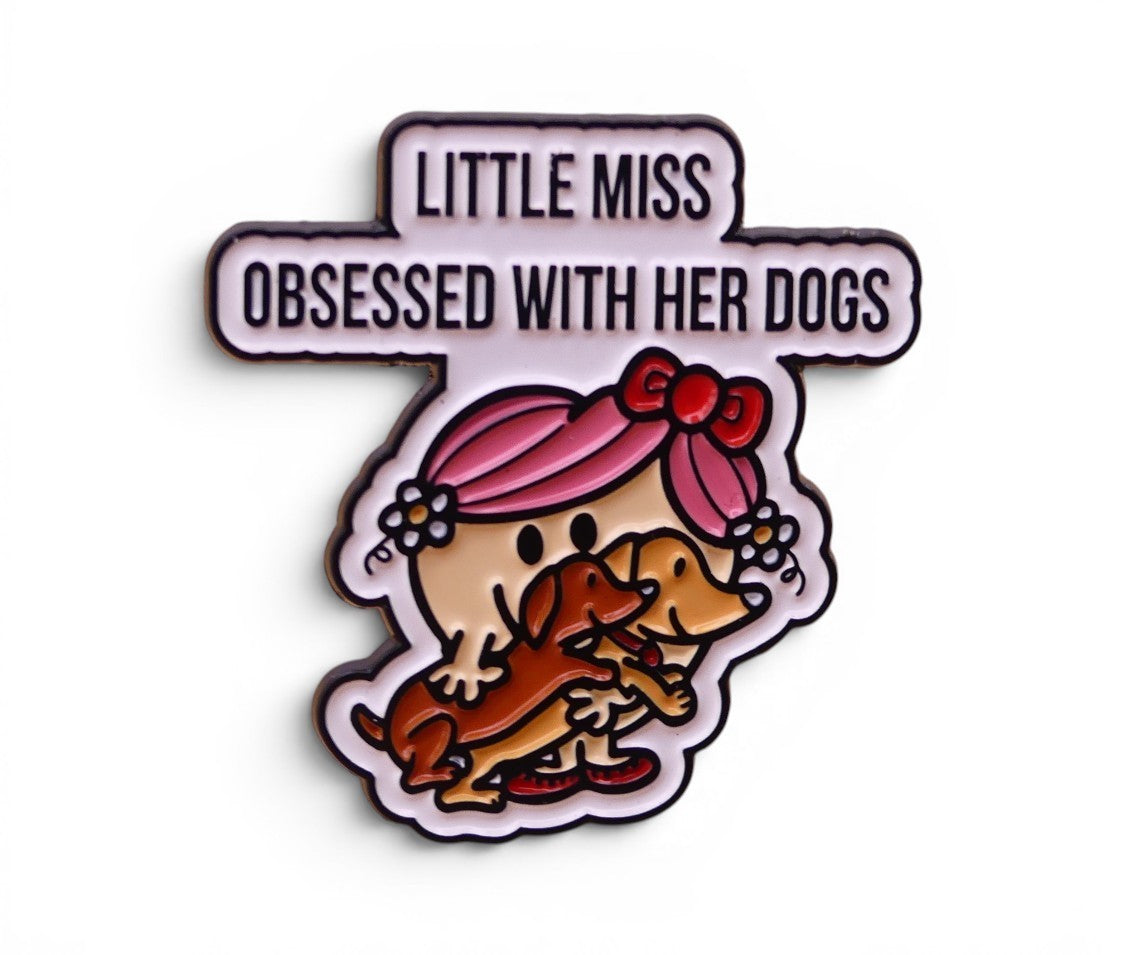 Enamel pin with 'Little Miss' character holding two dogs and text 'Obsessed with her dogs' 