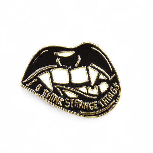 Lip-shaped pin with black interior and gold exterior, featuring text  i think strange things 