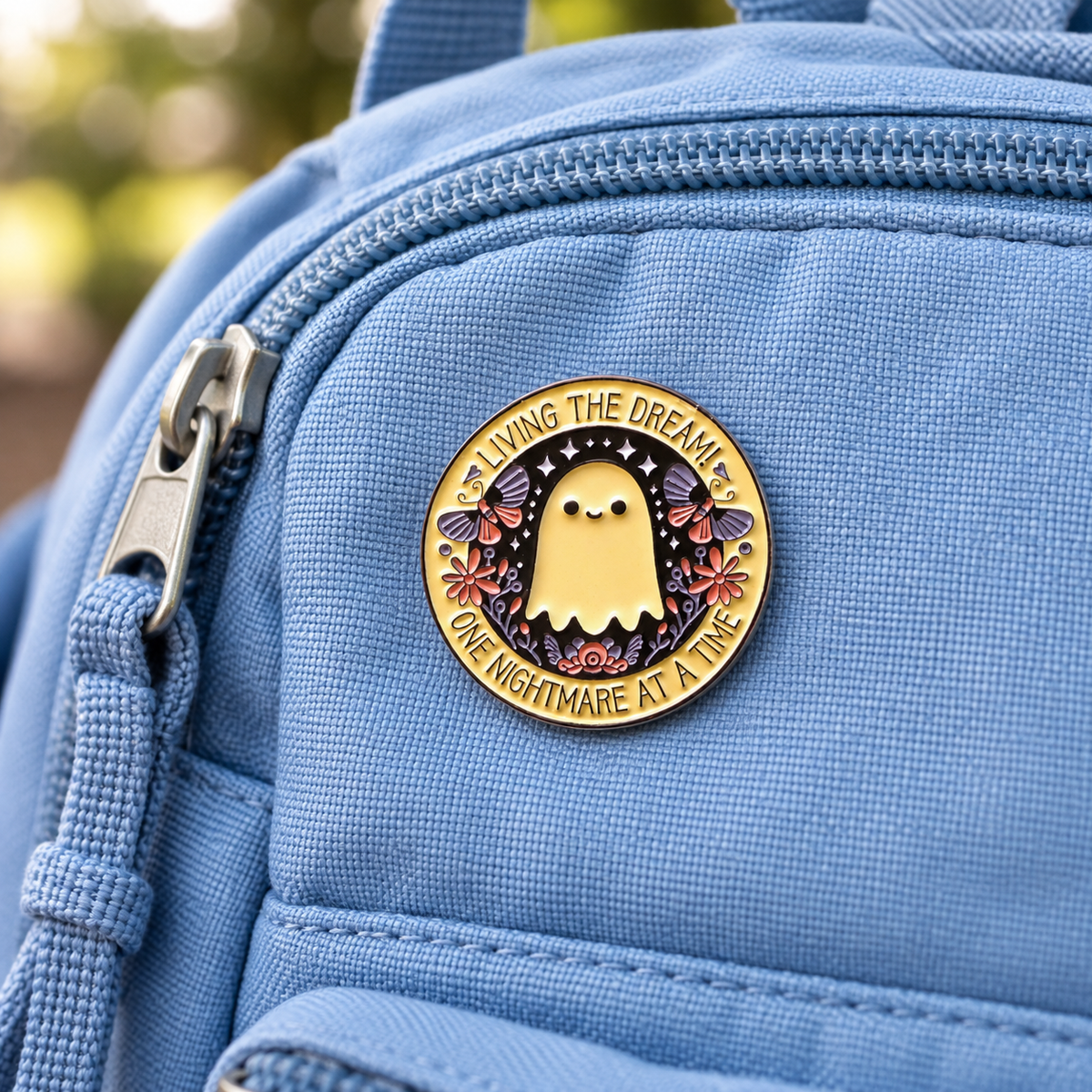 Enamel ghost pin badge with “Living the Dream” on blue backpack pocket