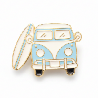 A retro camper van enamel pin badge in blue and white with a surfboard attached to the side.
